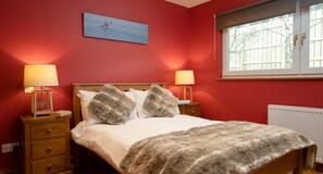 A bedroom with a bed, two bedside tables, a window, and a painting on the wall.