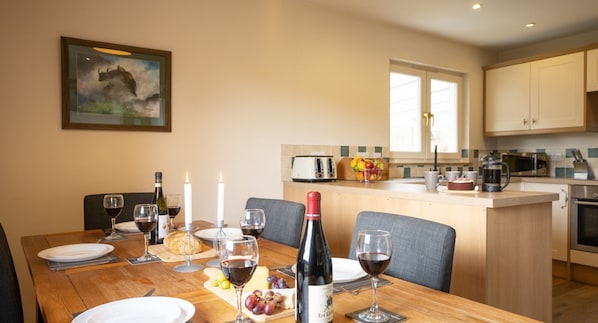 A dining area with a wooden table set for a meal, a kitchen in the background, and a framed picture on the wall.
