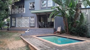 Ein zweistöckiges Haus mit Swimmingpool, einer überdachten Terrasse und einem Garten mit großen Bananenpflanzen.