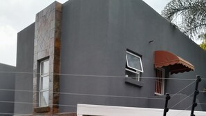 Ein modernes Gebäude mit grauer Fassade, weißem Balkongeländer und einem kleinen Fenster mit brauner Markise.