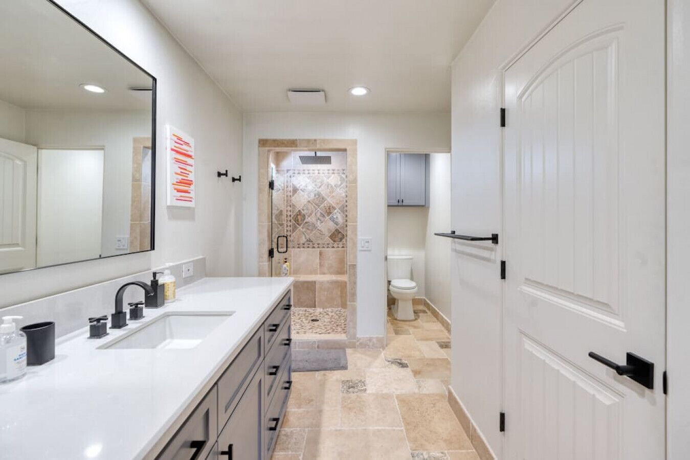 A modern bathroom with a double sink vanity, a shower with a tiled wall, and a toilet.