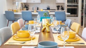 A modern dining area with a long table set for a meal, featuring yellow and blue chairs, and a central decorative golden sculpture. - The Orchid House - Palm Springs (Palm Springs)