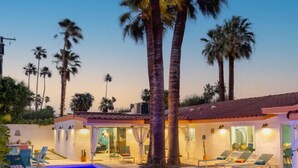 A swimming pool with lounge chairs, palm trees, and a building with a tiled roof. - The Orchid House - Palm Springs (Palm Springs)