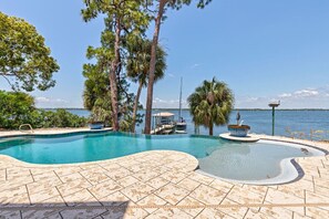 A swimming pool with a curved edge, surrounded by a tiled deck and palm trees. - Luxury Villa, Pool, Spa, Dock, Waterfront, Theater (Merritt Island)