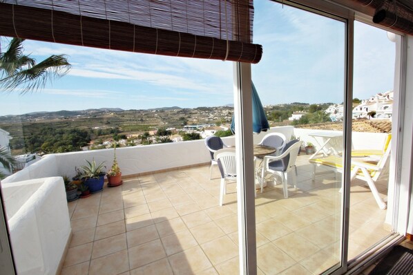 A balcony with a view of a hilly landscape, white chairs, and potted plants.