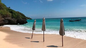A beach with three umbrellas and a boat in the water. - Villa Lumi with Private Pool - 3BR (Pecatu)