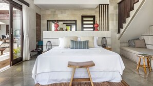 A modern bedroom with a large bed, a wooden stool, and a small table. - Villa Lumi with Private Pool - 3BR (Pecatu)