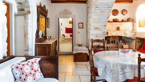 A rustic room with exposed stone walls, a wooden ceiling, a fireplace, a dining table with a white tablecloth, and a cozy seating area. - Zeus House Country Home with Mountain View, 2 Private Terraces & Wi-Fi (Naxos)