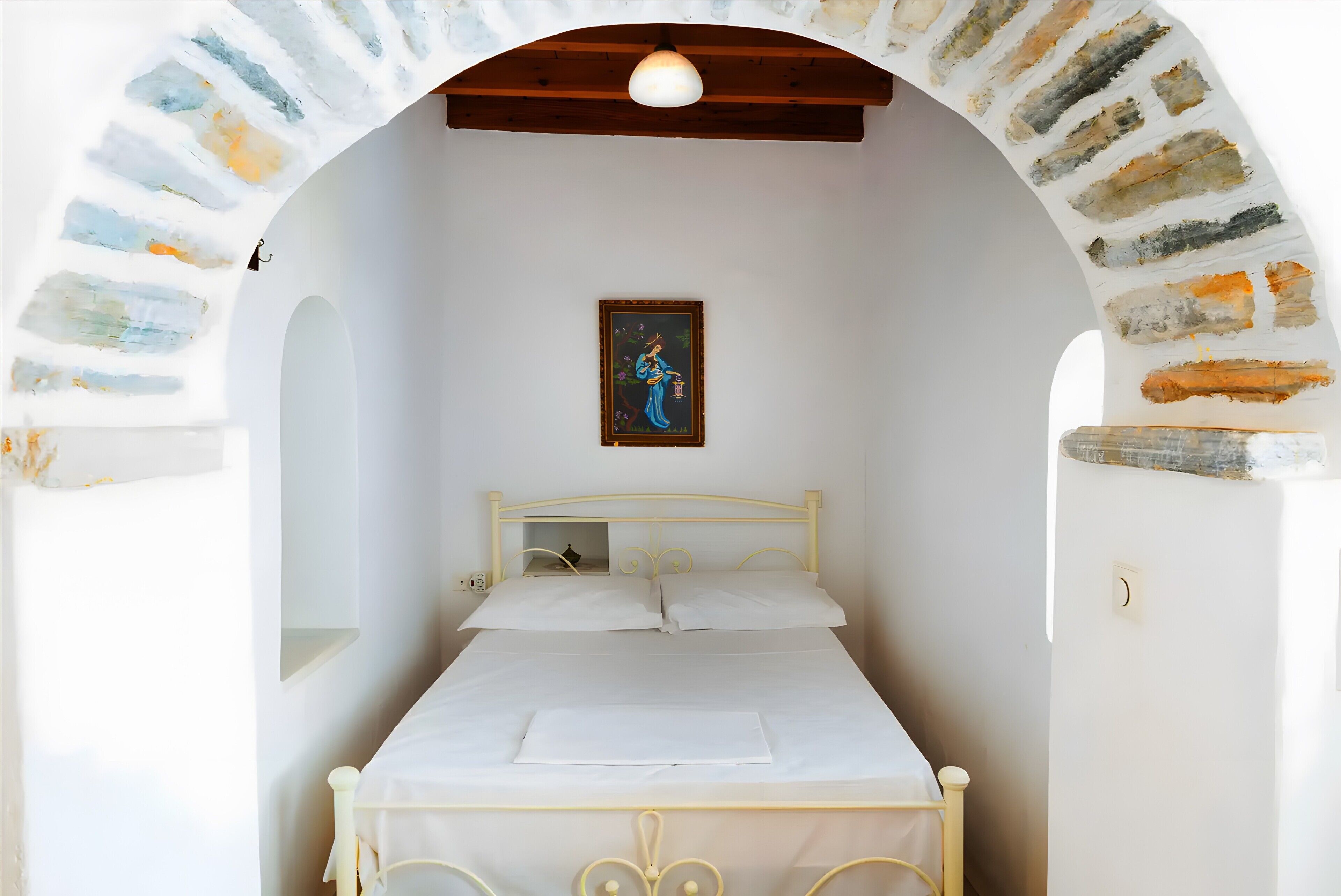 Un lit dans une chambre avec une arche en pierre, un tableau au mur et un luminaire au plafond.