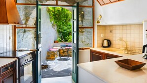A kitchen with stone walls, a wooden ceiling, and a view of a garden through an open door. - Zeus House Country Home with Mountain View, 2 Private Terraces & Wi-Fi (Naxos)