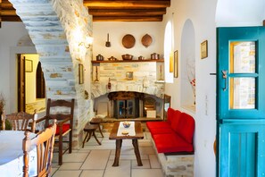 A stone fireplace, wooden furniture, and a red sofa in a room with white walls and a blue door.