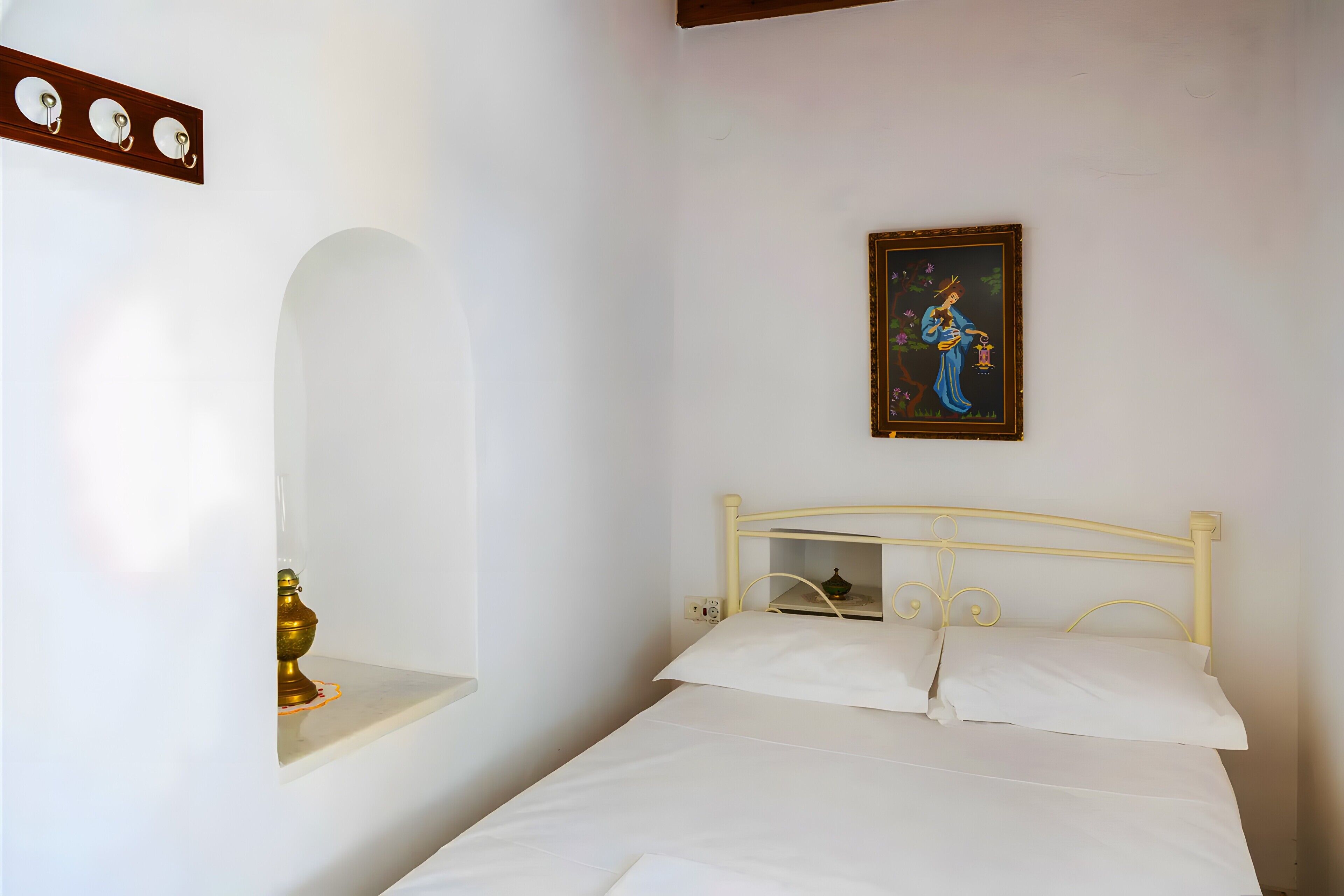 Une chambre à coucher avec un lit, une étagère fixée au mur sur laquelle se trouve un objet en laiton, un tableau et un luminaire fixé au mur.