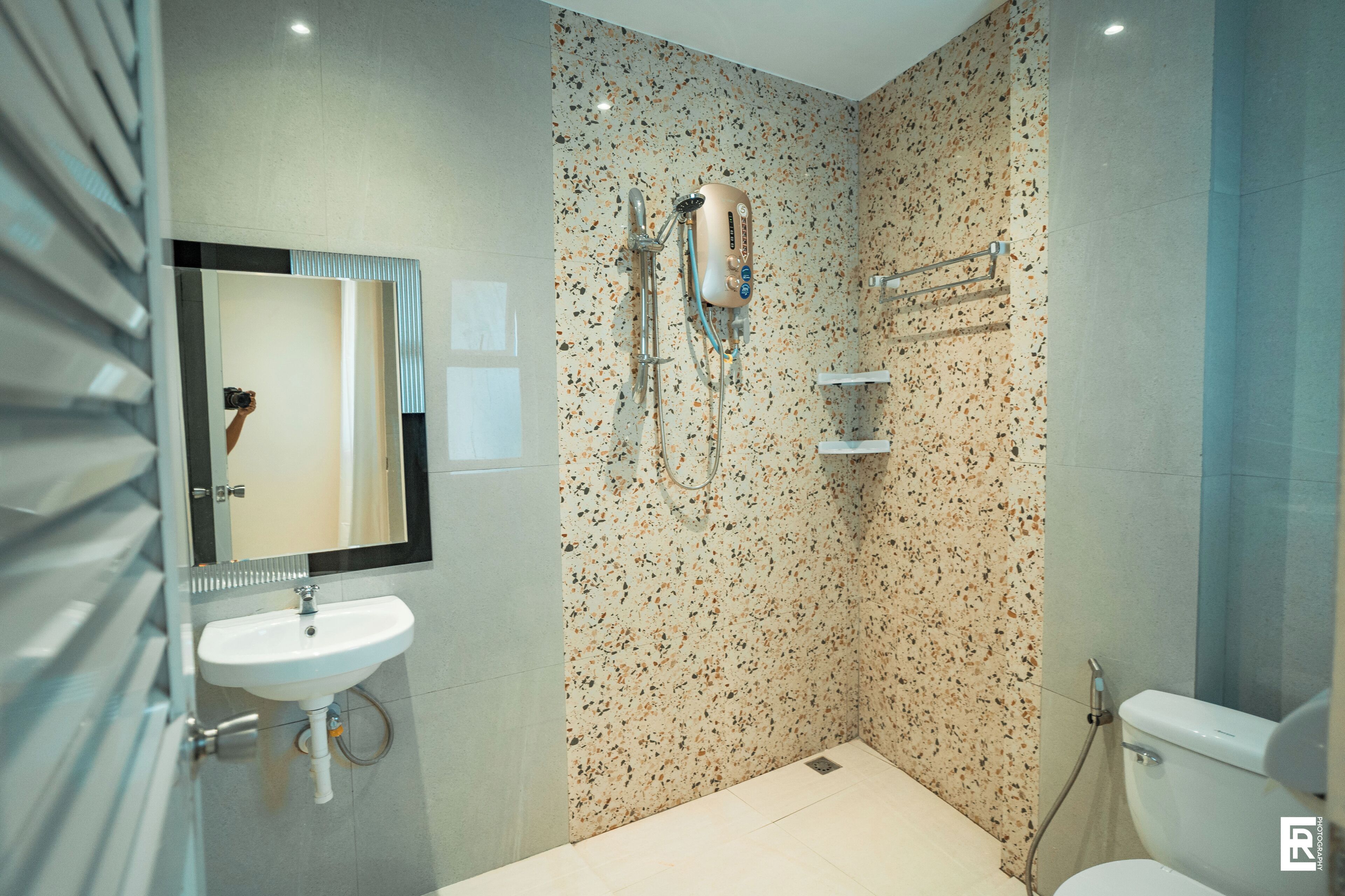 A modern bathroom with a white sink, a mirror, a shower with a handheld showerhead, and a toilet.
