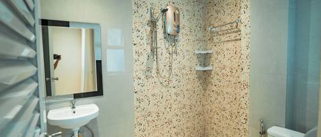 A modern bathroom with a white sink, a mirror, a shower with a handheld showerhead, and a toilet.