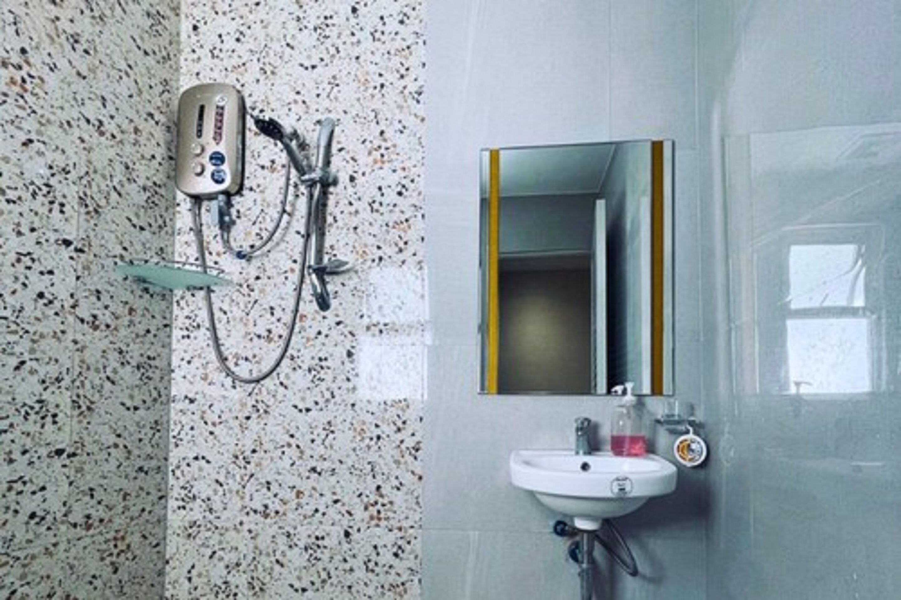 Ein Badezimmer mit einer Wand aus punktierten Fliesen, einer Handbrause, einem Waschbecken mit Spiegel und einem Seifenspender.