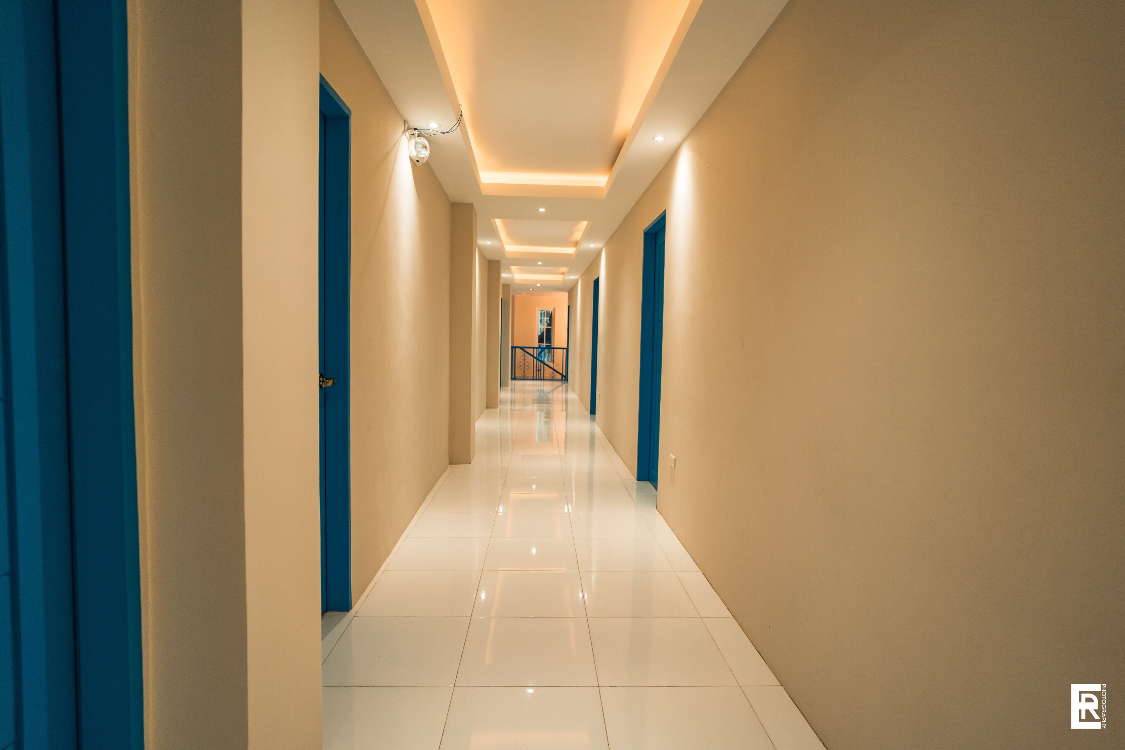 A hallway with a glossy white floor, blue doors, and recessed lighting.