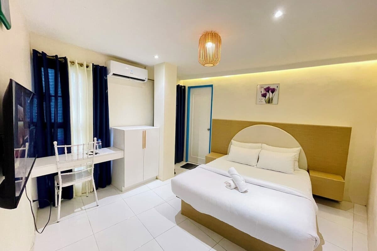 Una habitación de hotel con cama, escritorio con silla, armario y aire acondicionado.