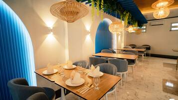 A modern restaurant interior with wooden tables, grey chairs, and hanging wicker lamps.
