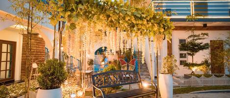 Un espacio exterior bien cuidado con un banco, plantas en macetas y un arco decorativo.