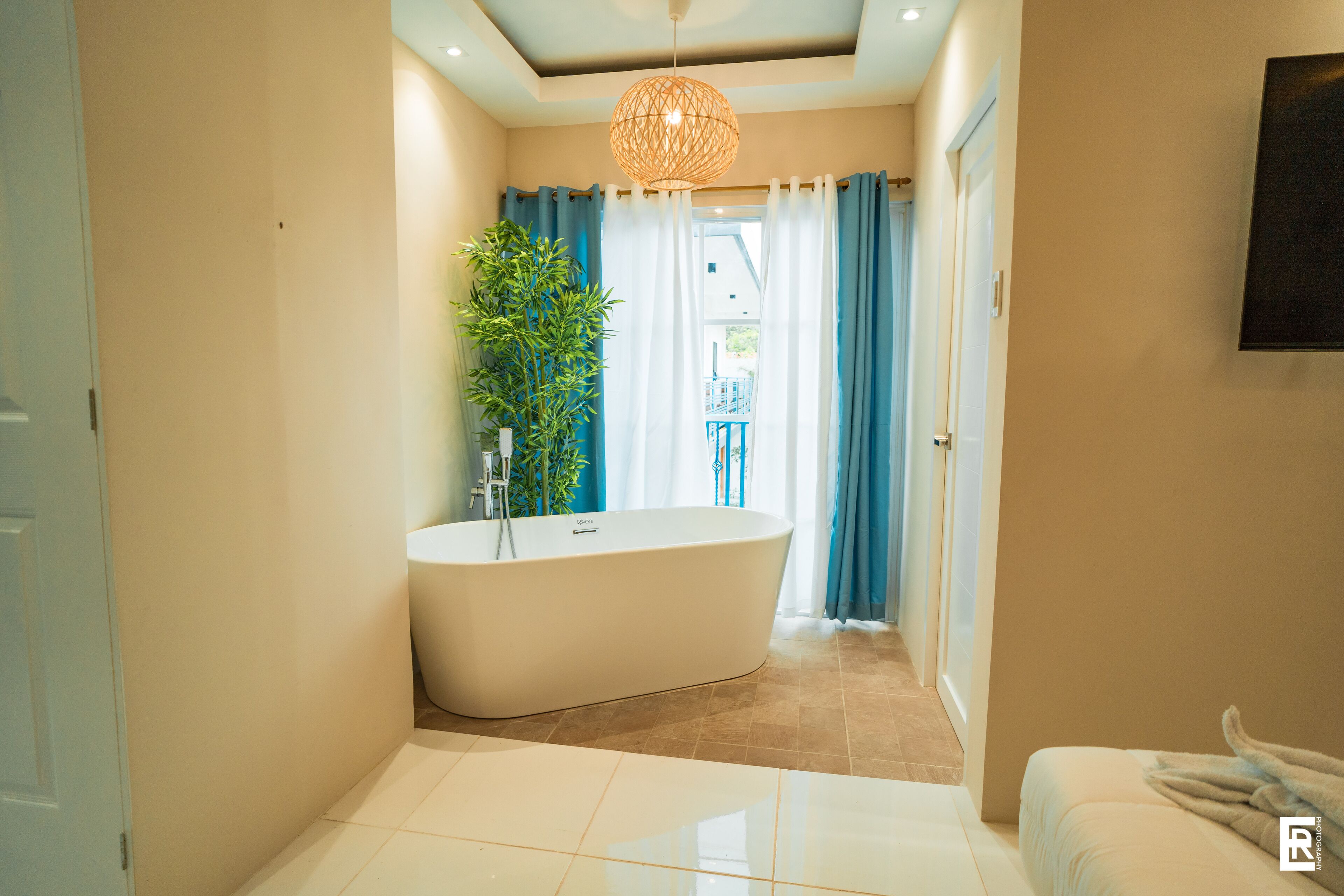 A modern bathroom with a freestanding bathtub, a potted plant, and a view of the outdoors through a glass door.