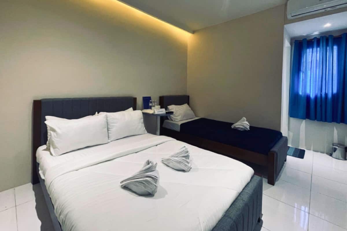 Una habitación de hotel con una cama grande, una cama más pequeña y una mesita de noche con una lámpara.