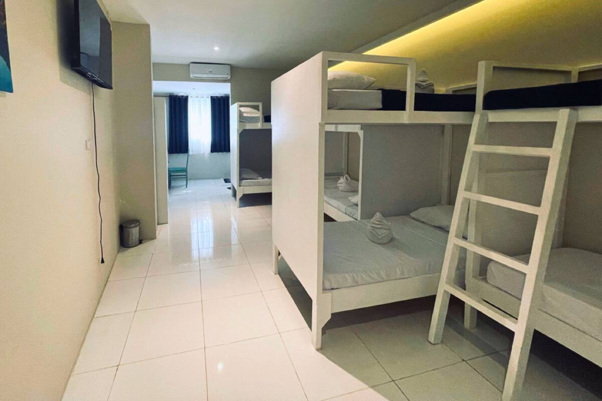 Habitación de hotel con literas, televisor montado en la pared y piso de baldosas.