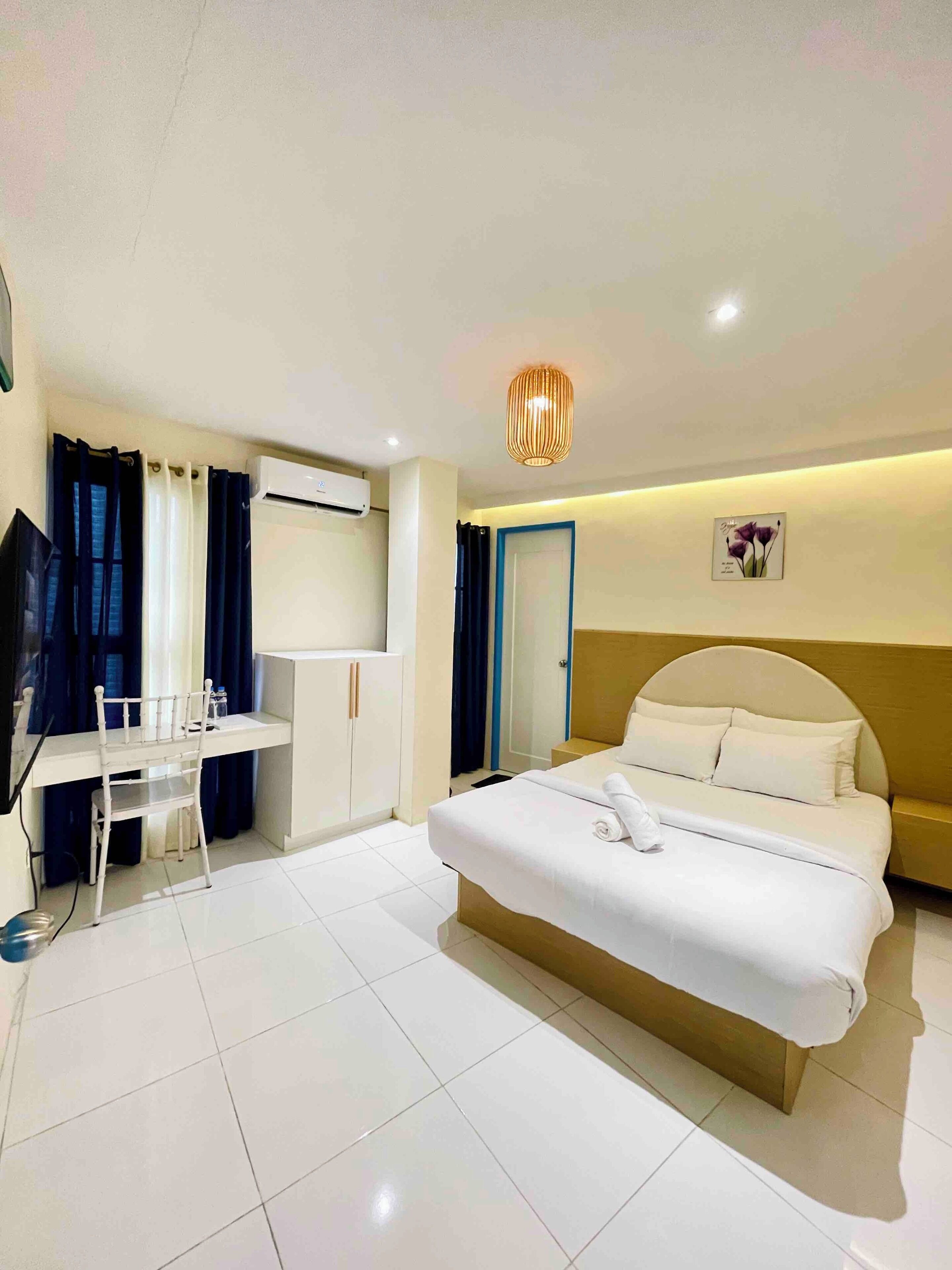 A modern hotel room with a large bed, a desk with a chair, a television, and an air conditioning unit.