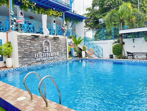 A swimming pool with a sign for Bernese Resort Hotel, surrounded by blue railings and greenery.