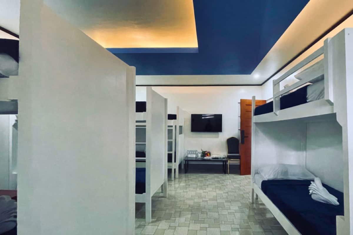 Habitación con literas, un televisor en la pared, una mesita pequeña y una puerta que da a otra habitación.