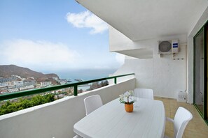 A balcony with a white table, chairs, and a potted orchid.
