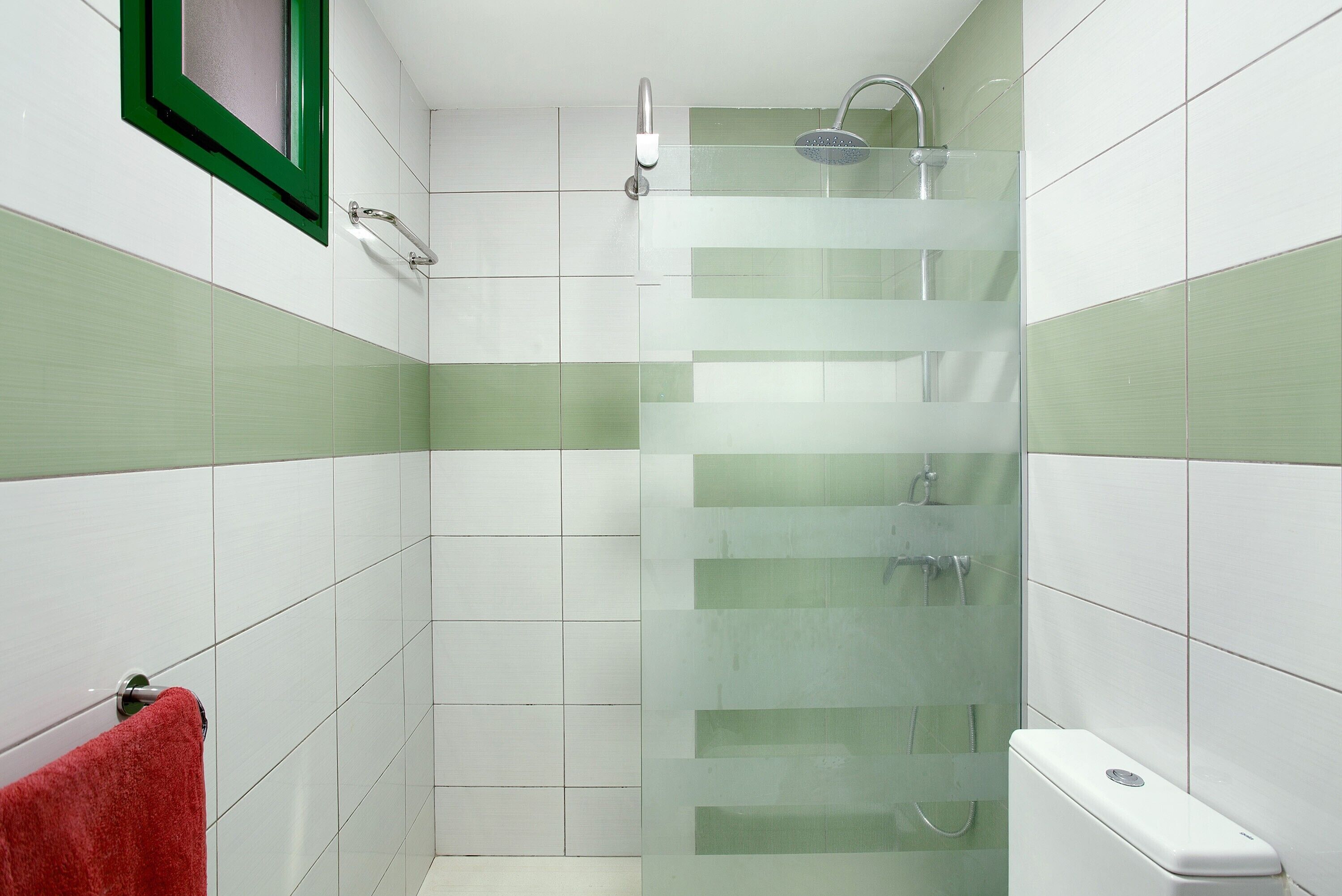 Un baño con cabina de ducha de vidrio, una toalla roja y un inodoro blanco.