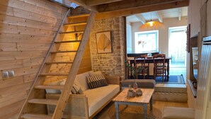A wooden interior with a staircase, a sofa, a coffee table, and a dining area with chairs and a table.