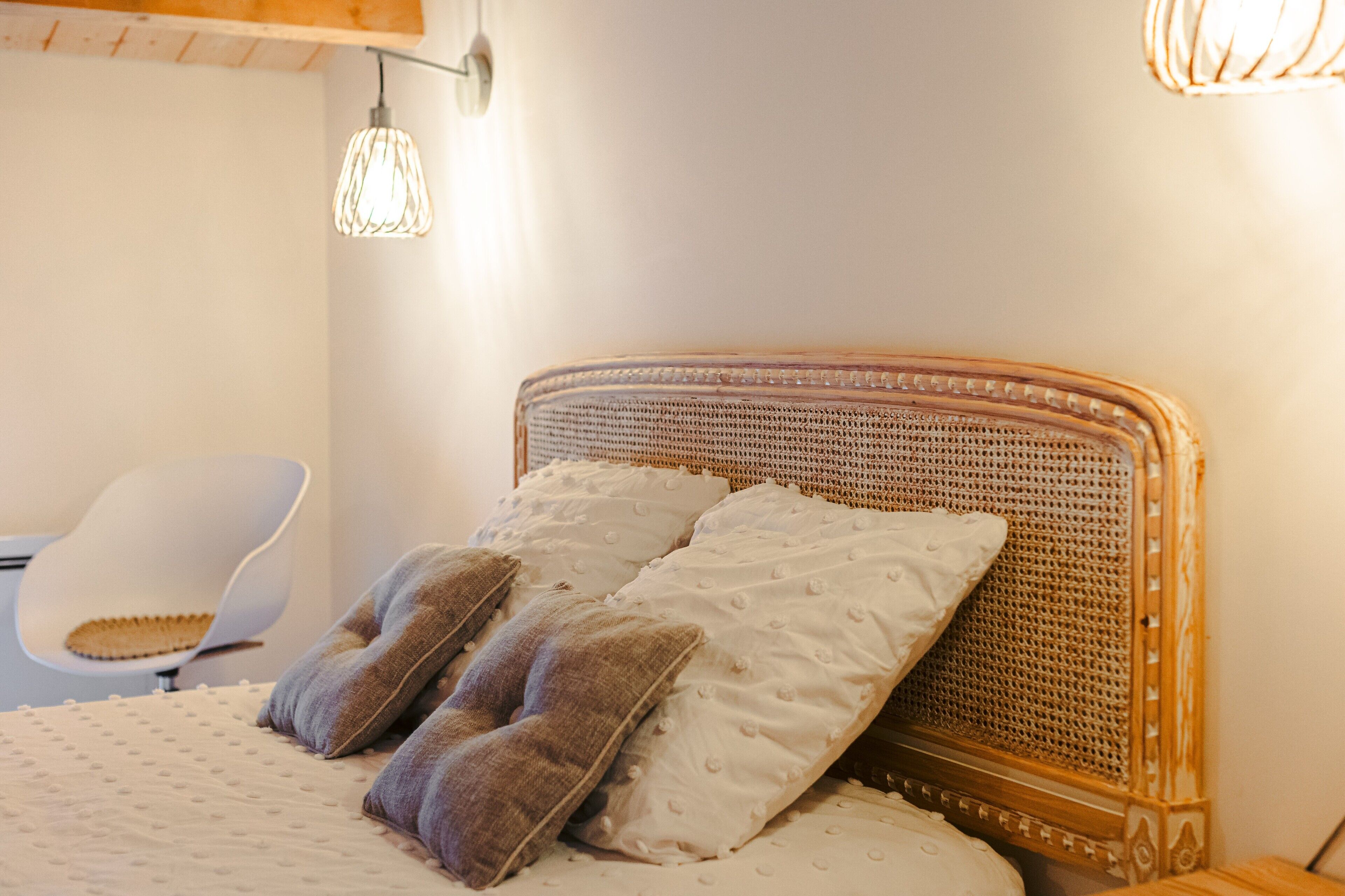 Un lit avec une tête de lit en osier, deux oreillers et un couvre-lit blanc à texture.