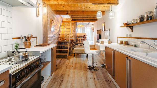 A kitchen with wooden beams, a stove, a chair, and a sink.