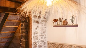 A rustic interior with a stone wall, wooden staircase, and a shelf with potted plants.