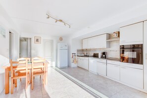 Une cuisine moderne avec des meubles blancs, un coin repas avec des chaises en bois et un four encastré.