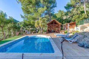 Une piscine avec des chaises longues, une terrasse en bois et une petite structure en bois dotée d’un toit.