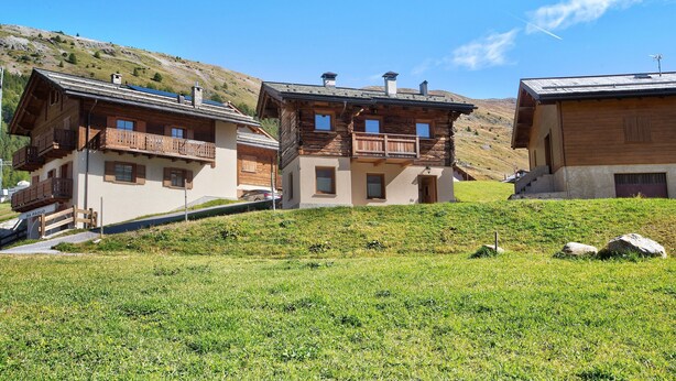 A cluster of wooden buildings with balconies, set against a hillside backdrop. - Apartment 'Al Baitin Trepalle' with Mountain View (Livigno)