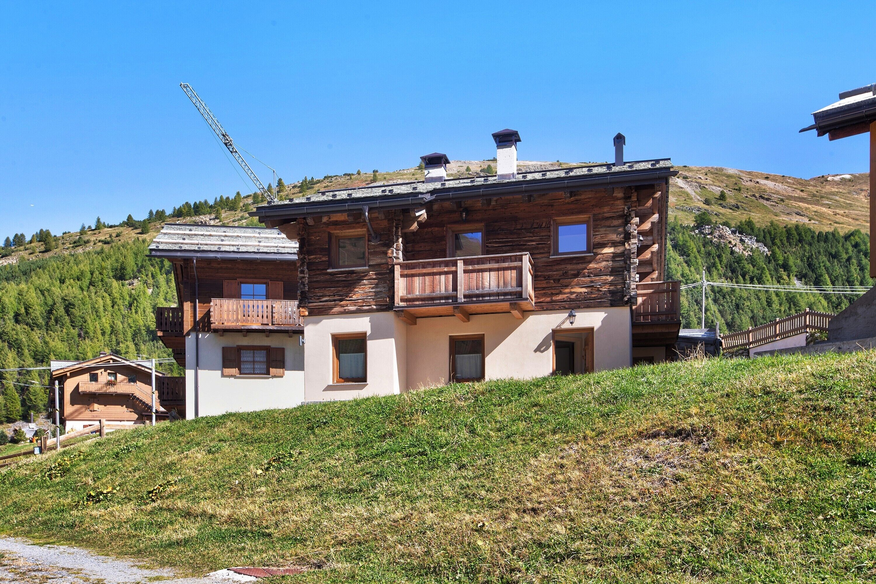 Un chalet en bois à deux étages, doté d’un balcon, situé sur une colline sous un ciel dégagé.