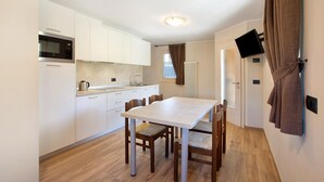 A compact kitchen with white cabinets, a microwave, a dining table with chairs, and a television mounted on the wall. - Apartment 'Al Baitin Trepalle' with Mountain View (Livigno)