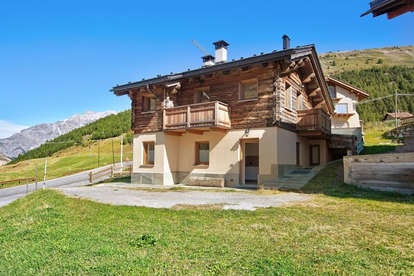 A wooden chalet with a balcony, a stone staircase, and a view of mountains.