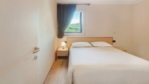 A hotel room with a bed, a nightstand, a window with a view, and a door. - Apartment 'Al Baitin Trepalle' with Mountain View (Livigno)