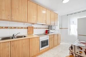 Una cocina con armarios de madera, un lavamanos de acero inoxidable, un microondas y un horno empotrado.
