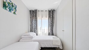 A bedroom with two beds, a window with sheer curtains, a door, and a wall-mounted cactus artwork.