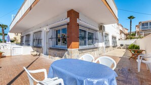 A covered patio area with a table and chairs, a brick wall, and a white railing. - Apartment 'Las Calas Deluxe B' with Shared Pool, Private Terrace and Wi-Fi (Torrevieja)