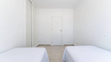 Una habitación con dos camas individuales, una puerta blanca y suelo de baldosas.