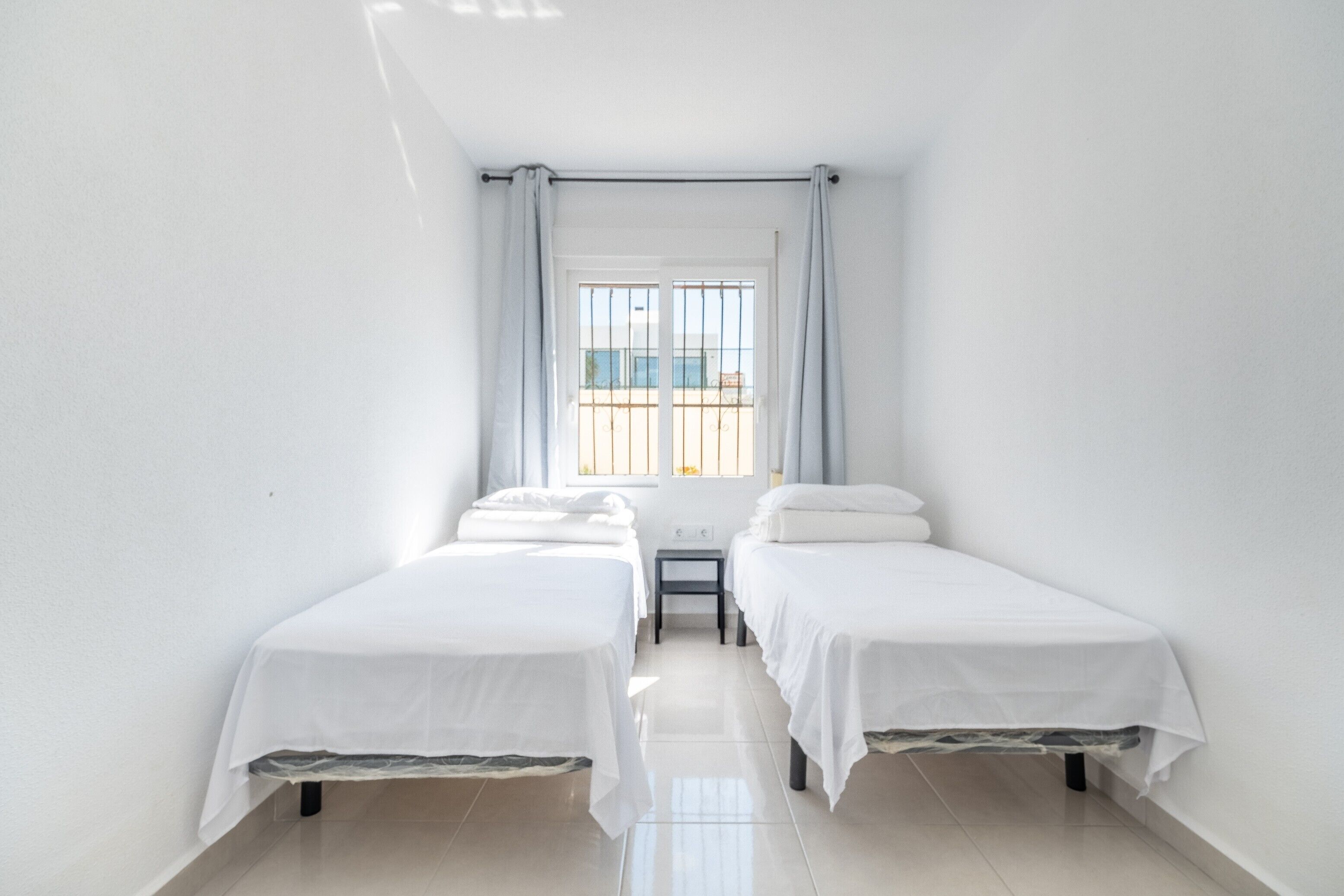 Een kamer met twee eenpersoonsbedden, een tafeltje en een raam met gordijnen.