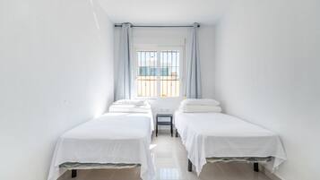 Een kamer met twee eenpersoonsbedden, een tafeltje en een raam met gordijnen.