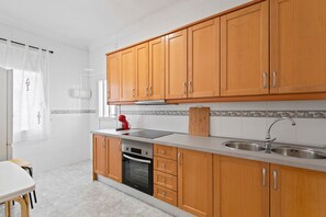A kitchen with wooden cabinets, a stainless steel sink, a red kettle, and a tiled backsplash. - Apartment 'Las Calas con Terraza C' with Shared Pool, Private Terrace and Wi-Fi (Torrevieja)