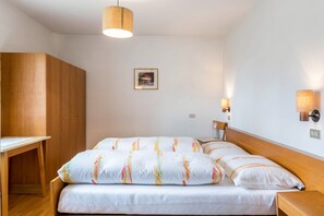 A bedroom with a bed, wooden wardrobe, bedside tables, wall-mounted lamps, and a framed picture on the wall.
